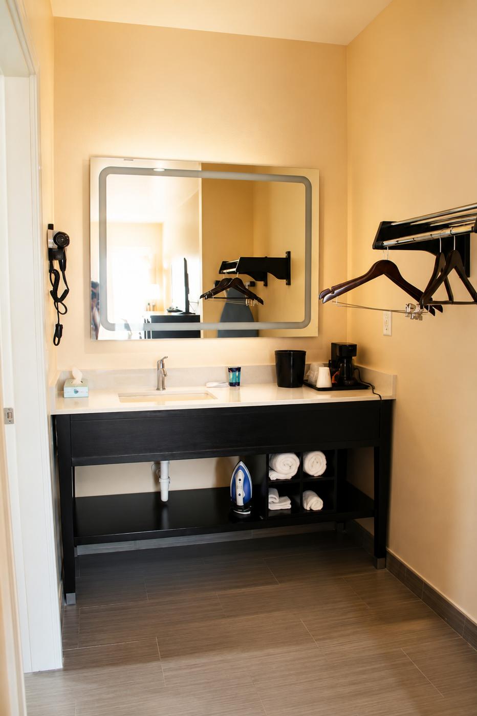 Modern bathroom vanity with lighted mirror, hairdryer, coffee maker, and folded towels